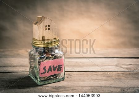 Wooden house on jar of coins with the word save. Saving concept. Vintage tone photo.
