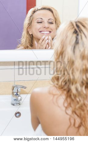 Positive and Sensual Caucasian Blond Woman Looking in Mirror and Examining Her Face. Vertical Image Composition