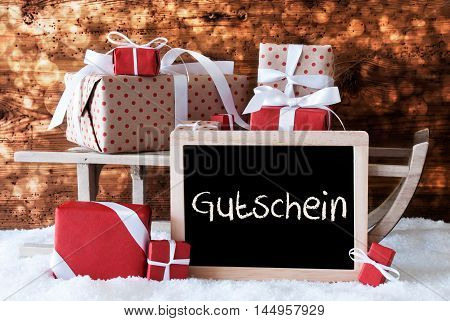 Chalkboard With German Text Gutschein Means Voucher. Sled With Christmas And Winter Decoration. Gifts And Presents On Snow With Wooden Background And Bokeh Effect.