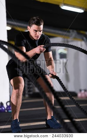 young fit athlete man working out in functional training gym doing  battle ropes exercise as part of cross fitness training