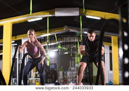 young fit sports couple working out in functional training gym doing  battle ropes cross fitness exercise