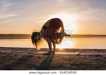 Silhouette Woman On The Beach At Sunset Doing Yoga Asana. Morning Natural Stretch Warm-up Training