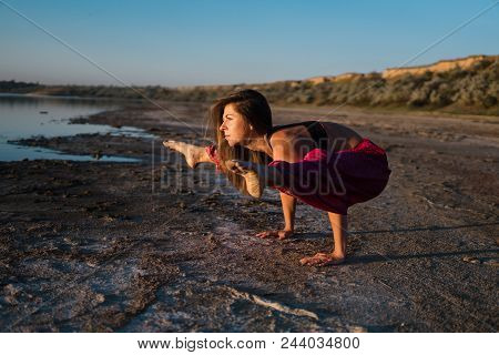 Woman On The Beach At Sunset Doing Yoga Asana. Morning Natural Stretch Warm-up Training