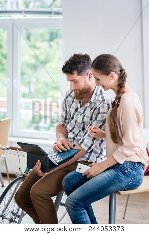 Cheerful young man using a tablet with keyboard and wireless connection to internet, while collaborating with his female co-worker in a shared co-working office space