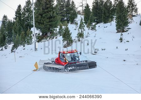 Red Pisten Bully Cleaning Snow On Winter Mountain With Pine Tree Background