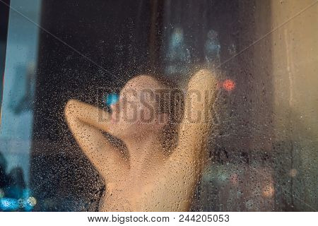 Beautiful Woman In The Shower Behind Glass With Drops On The Background Of A Window With A Panoramic