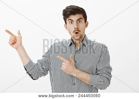 Portrait Of Flirty Funny European Male Model With Moustache And Beard In Striped Shirt, Pointing Lef
