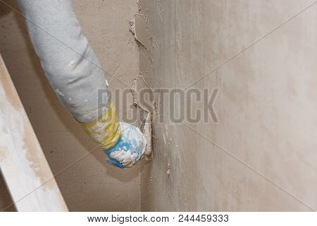 Hand With A Spatula In The Process Of Leveling The Raw Plaster.