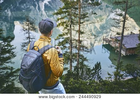 Young Man (tourist) With Backpack Is Walking Throught Forest. Mountains Refelection In Lake Braies, 