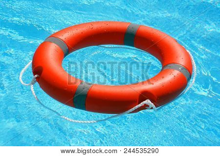 Red Lifebuoy Pool Ring Float On Blue Water. Life Ring Floating On Top Of Sunny Blue Water. Life Ring