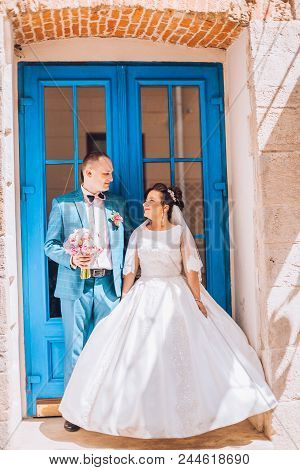 Happy Bride And Groom After Wedding Ceremony In The Background Old Door. Newlyweds Look To Each Othe
