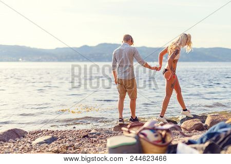 Happy Couple In Love Holding Hands And Walking At The Beach. Summer Flirt In Bathing Clothes And Bik