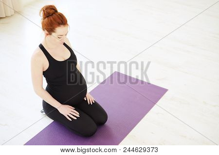 Smiling Cute Pregnant Woman Resting After Pilates Class While Sitting On A Mat With Bent Legs. Prena