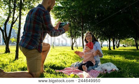 Happy Family Is Laying On The Pled And Doing Selfie With A Baby At Sunset In The Park. Father Takes 