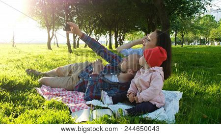 Happy Family Is Laying On The Pled And Doing Selfie With A Baby At Sunset In The Park. Father Takes 