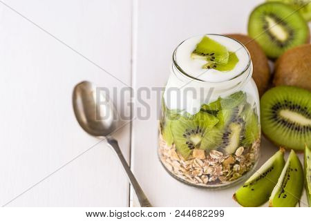 White Yogurt With Muesli In Glass Bowl With Pieces Of Kiwi On Top And Whole Pieces On The Right Side