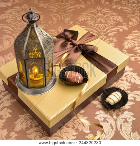 Traditional fanoos or an Arabic decorative lantern placed on top of golden gift box along with date chocolates. Eid celebration objects and background.