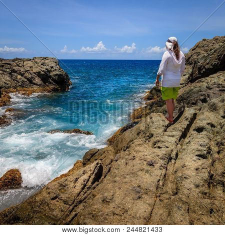A woman standing on a cliff and watching surf on an island in BVI