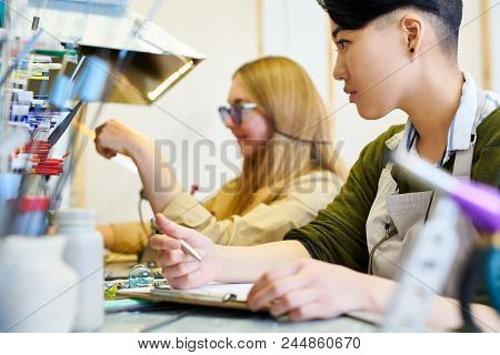 Side View Portrait Of  Young Asian Woman Drawing Sketches Sitting At Table In Creative Studio , Copy