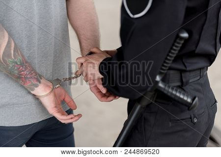 Cropped Shot Of Policewoman With Truncheon Handcuffing Bandit