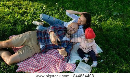 Happy Family Is Laying On The Pled And Doing Selfie With A Baby At Sunset In The Park. Father And Mo