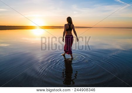 Silhouette Woman On The Beach At Sunset . She Stands In Water. Morning Natural Stretch Warm-up Train