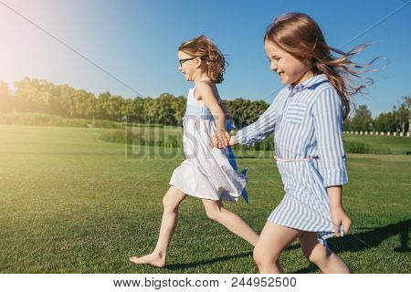 Two Joyfull Girls Running On The Field. Summer Activity And Leisure. Sisters.