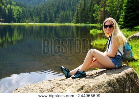 Tourist sitting on stone by moraine lake Kleiner Arbersee in National park Bavarian forest. Germany.