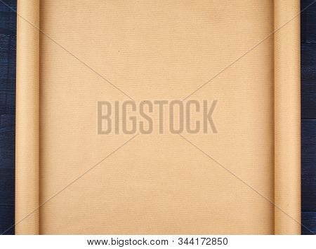 Untwisted Roll Of Brown Craft Paper On A Blue Wooden Background, Empty Space. Old Craft Paper Textur