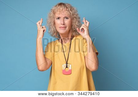 Senior Caucasian Woman In Yellow Clothes Crossing Fingers Wishing Luck
