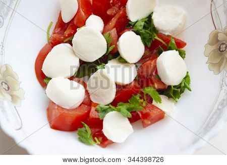 Salad With Slices Of Tomato, Mozzarella And Parsley On A White Plate