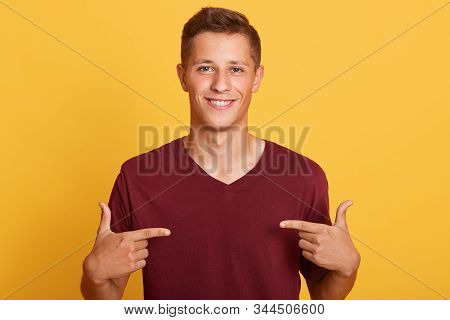 Close Up Of Handsome Man In Blank Burgundy T Hirt Pointing At Himself Isolated Over Yellow Studio Ba