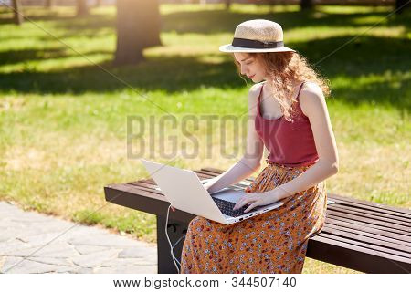 Outdoor Shot Of Girl Looking For Information Via Laptop And Wireless Internet, Charges With Help Of 