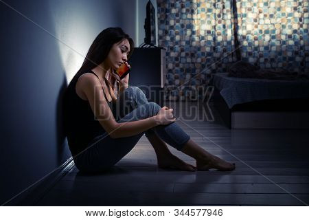 The Concept Of Domestic Violence. Exhausted Caucasian Woman Sits On The Floor In A Dark Room, Agains