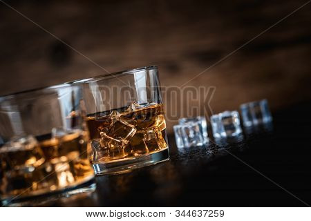 Whisky, Whiskey, Bourbon Or Cognac With Ice Cudes On Black Stone Table And Wood Background