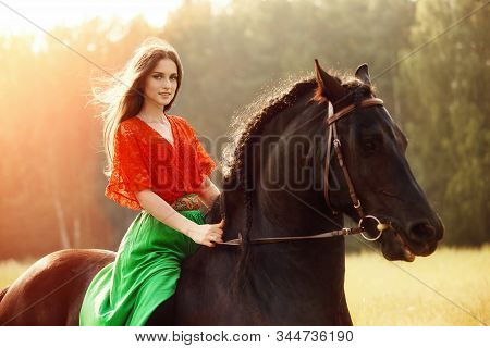 Gypsy Girl Rides A Horse In A Field In The Summer. A Woman With Long Hair Strokes And Caresses A Hor