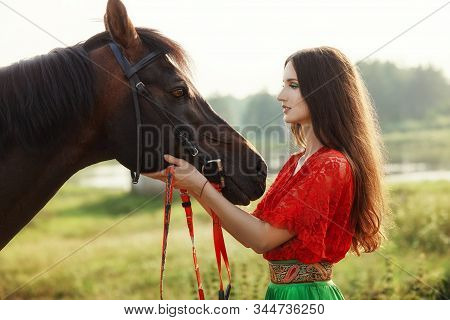 Gypsy Girl Rides A Horse In A Field In The Summer. A Woman With Long Hair Strokes And Caresses A Hor