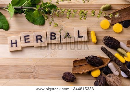 Herbal Word Written On Wooden Blocks With Scattered Medicines And Spices On A Wooden Background. Her