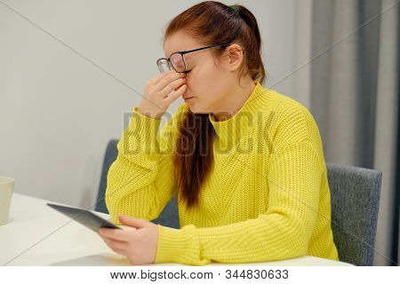 Young Caucasian Female In Glasses And Knitted Sweater Doing The Nose Massage When Reading Electronic