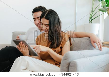 Asian Young Smiling Couple Drinking Coffee And Watching Online Movie Stream With Digital Tablet Rela