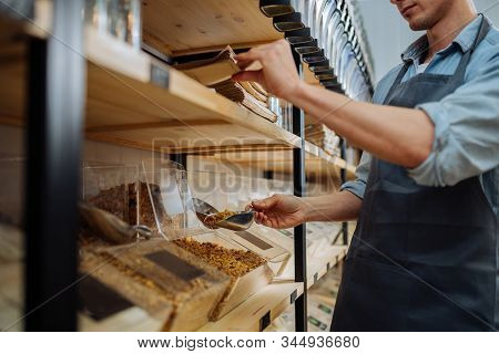 Close Up Of Hands Unrecognizable Male Worker Shop Assistant Filling Paper Bag With Oat Granola In Bu