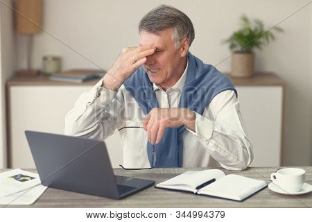 Tired Aged Man Massaging Nosebridge Holding Eyeglasses Working On Laptop In Modern Office. Selective