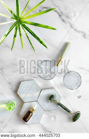 Self Made Moisturizer And Green Jade Face Roller And Essential Oil On Marble Cutting Board On Stone 