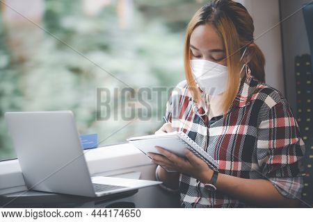Businesswoman Wearing A Mask And Working On Laptop On A Train, Asian Freelance Writer Or Designer Wr