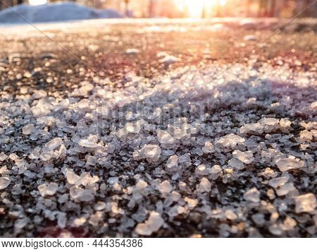Salt Grains On Icy Sidewalk Surface In The Winter. Applying Salt To Keep Road Clear And People Safe 
