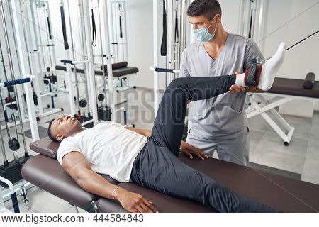 Experienced Physiotherapist Applying Gym Equipment For Patient Leg Rehabilitation