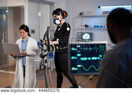 Athlete Sportwoman With Electrodes Attached To Her Body Running On Cross Trainer Doing Cardio Exerci