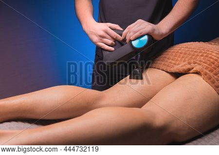 Male Masseur Doing Massage Exercises On The Thighs With The Help Of A Percussion Vibro Massager To A