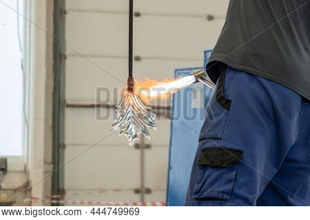 A Man Uses A Gas Burner To Melt Glass. A Craftsman Makes A Glass In A Leaf Shaped.