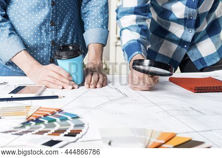 Man Carefully Studying Technical Drawing With Magnifying Glass. Designers Working With Color Swatche